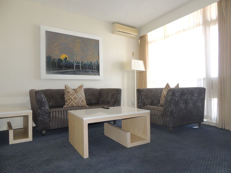 A living room featuring a large window for natural light, wall-mounted air conditioning, and carpeted flooring.
