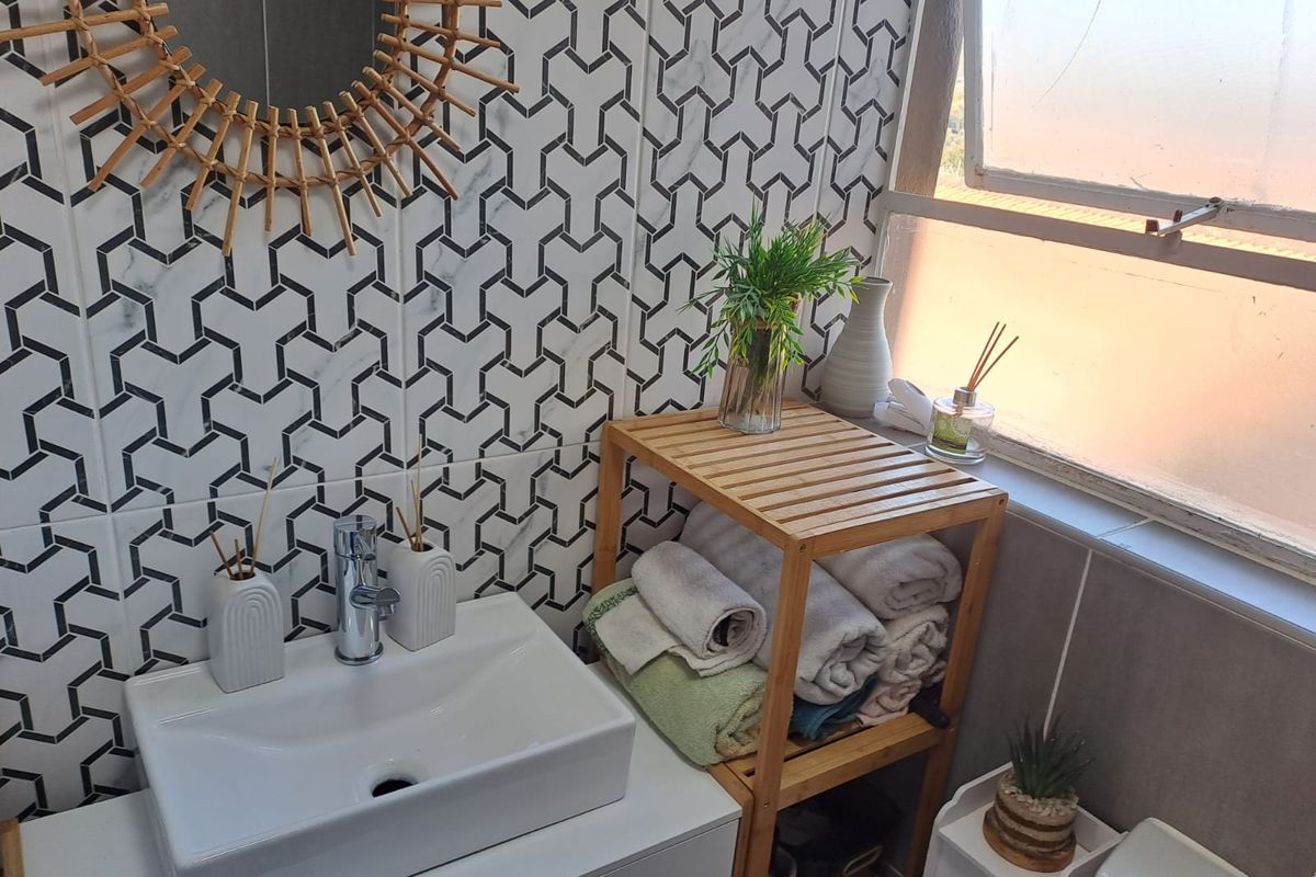 A modern bathroom featuring a white basin with a chrome faucet, geometric patterned wall tiles, and a window providing natural light.