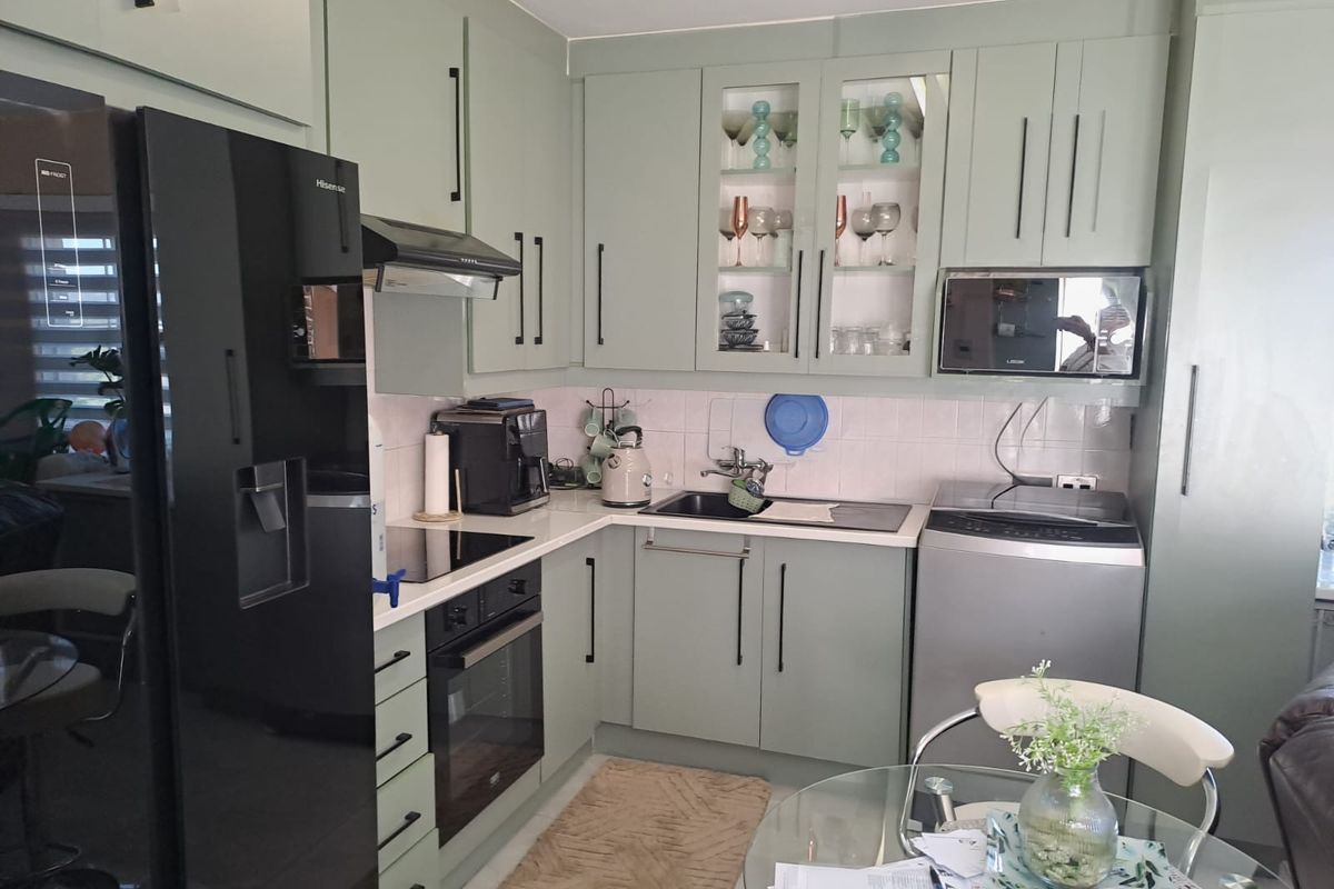 A well-maintained kitchen featuring sage green cabinetry, integrated appliances, a built-in oven, hob, and a tiled backsplash.