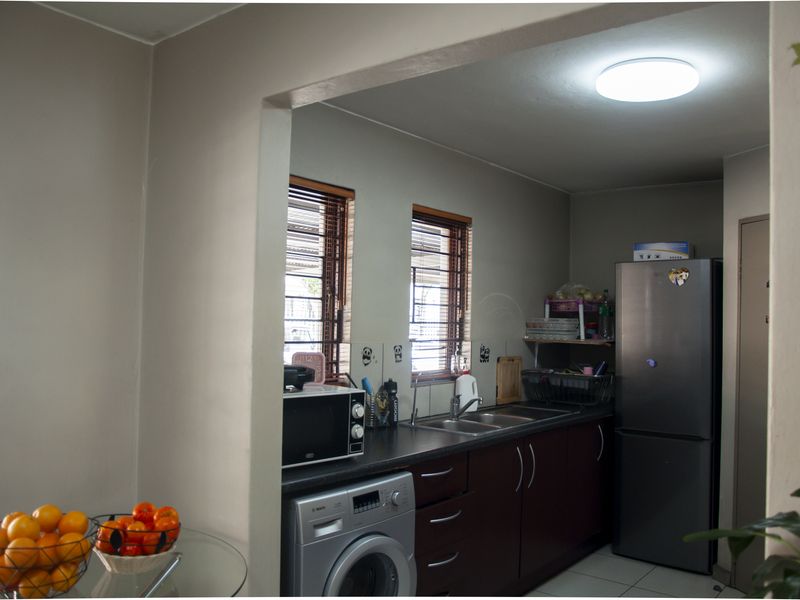A functional kitchen featuring dark cabinetry, a double sink, and integrated laundry appliance space, connected to an adjacent living area.