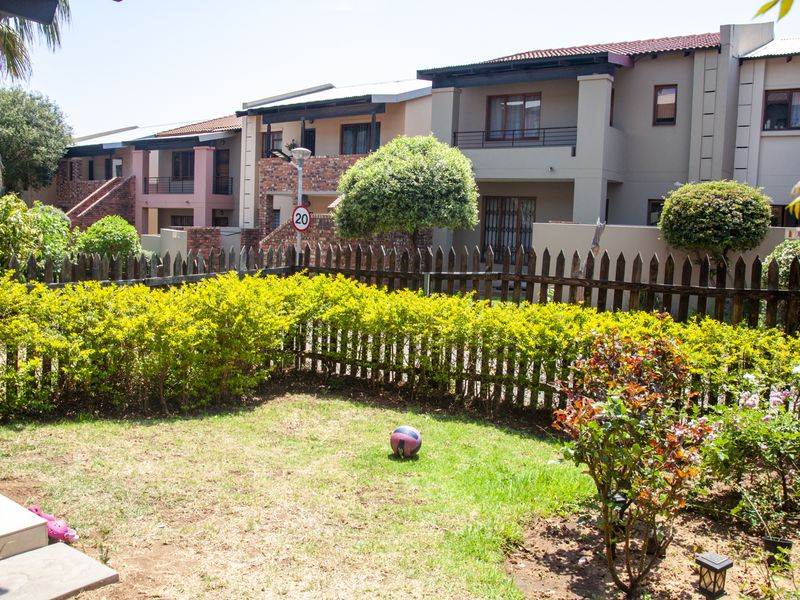 A view of a private garden area with a lawn and established shrubs, set against the rear facade of a townhouse complex.