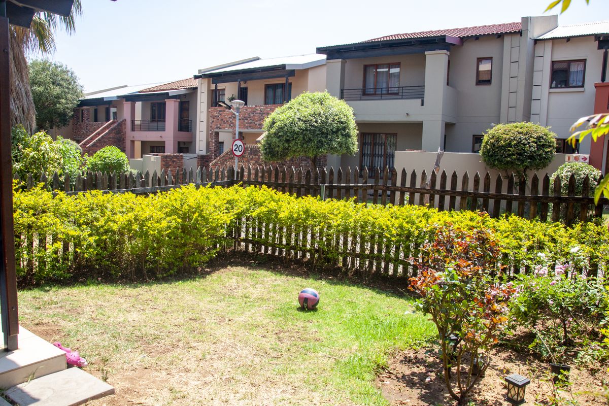 A view of a private garden area with a lawn and established shrubs, set against the rear facade of a townhouse complex.