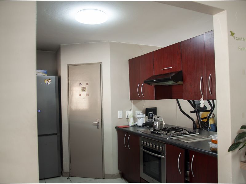 A compact kitchen featuring dark wood cabinetry, a built-in oven, gas hob, and extractor fan, with tiled flooring and a neutral wall finish.