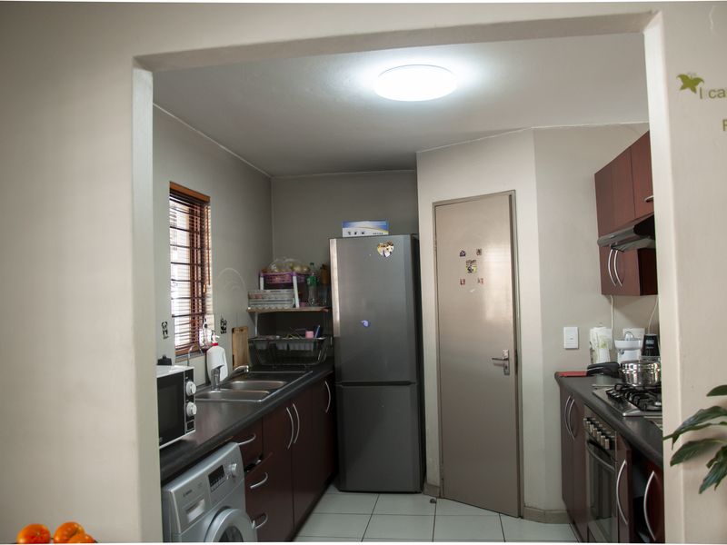 A functional kitchen featuring dark cabinetry, a built-in oven, gas hob, extractor fan, and a double sink with tiled flooring.