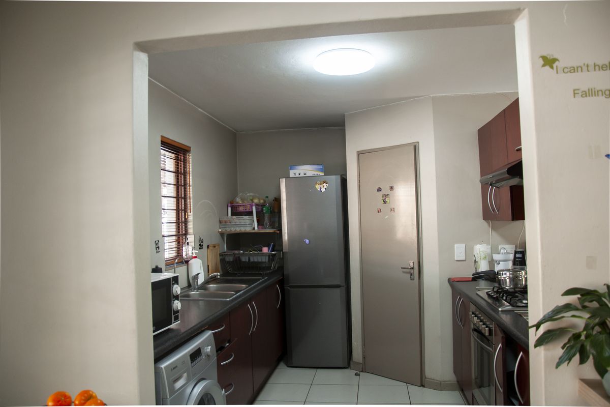 A functional kitchen featuring dark cabinetry, a built-in oven, gas hob, extractor fan, and a double sink with tiled flooring.