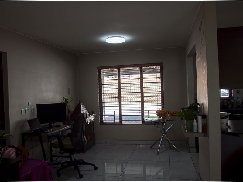 A living area featuring tiled flooring and a large window with horizontal blinds, providing natural light and a view of the exterior.