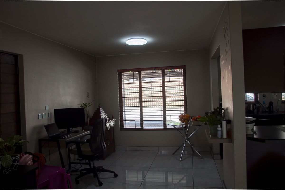 A living area featuring tiled flooring and a large window with horizontal blinds, providing natural light and a view of the exterior.