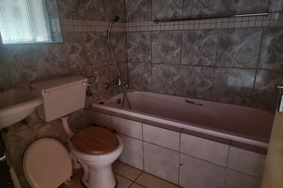 A dated bathroom featuring a bathtub with shower mixer, toilet, and washbasin, finished with marble-effect wall tiles and floor tiles.