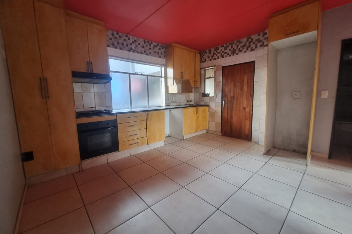 A functional kitchen featuring built-in wooden cabinetry, tiled flooring, a built-in oven and hob, and a dedicated space for a refrigerator.