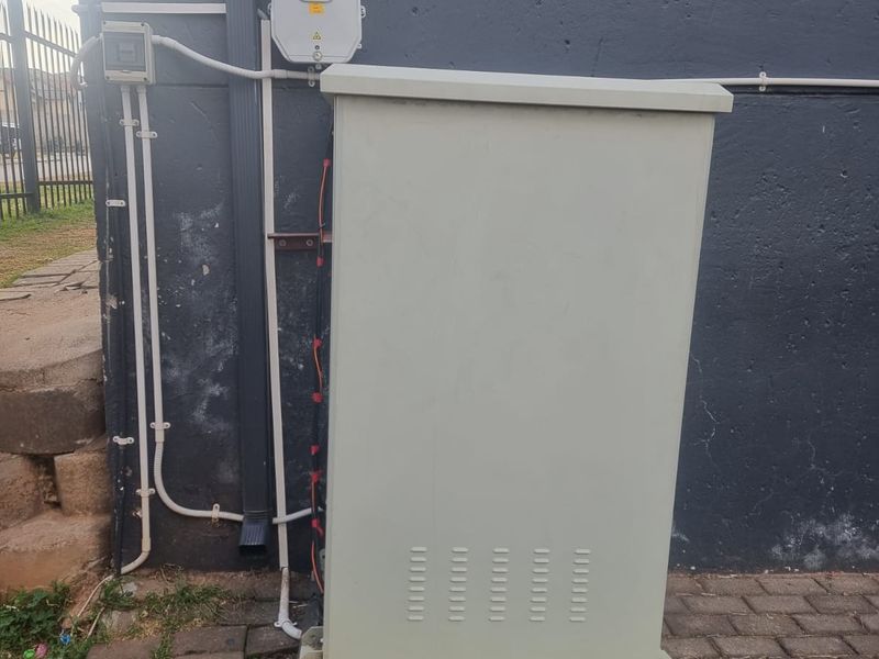 Exterior utility area featuring an electrical distribution box and external power supply unit mounted against a painted brick wall.