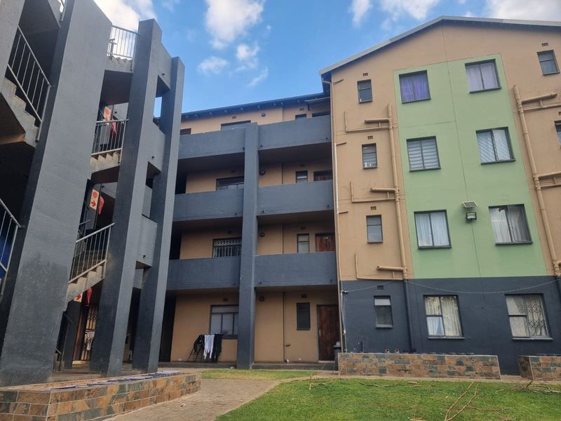 Exterior view of a multi-story apartment complex featuring concrete staircases, balconies, and a shared courtyard area with paved walkways.