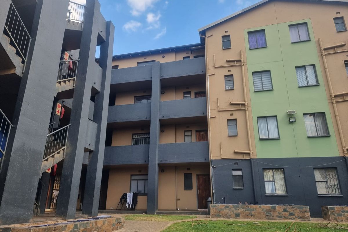 Exterior view of a multi-story apartment complex featuring concrete staircases, balconies, and a shared courtyard area with paved walkways.