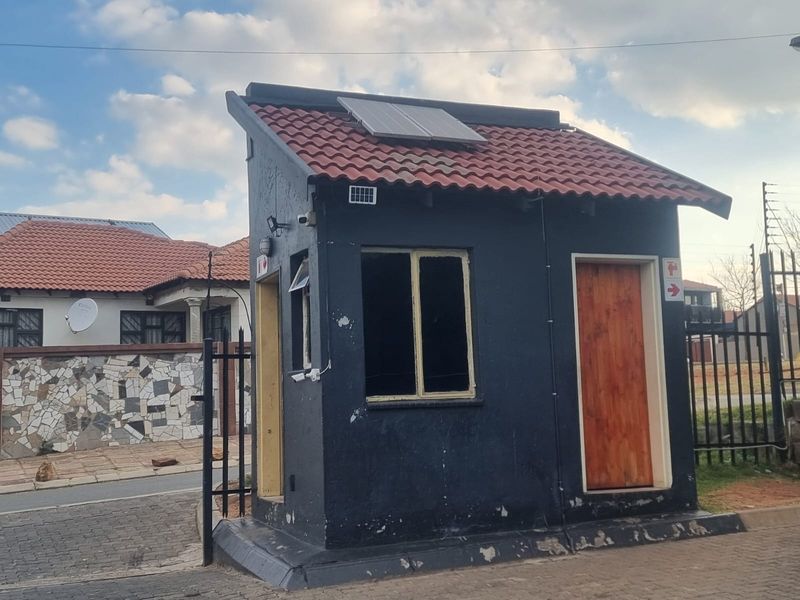 A small security guard house or utility structure featuring a tiled roof, solar panel, and paved surroundings within a residential complex.