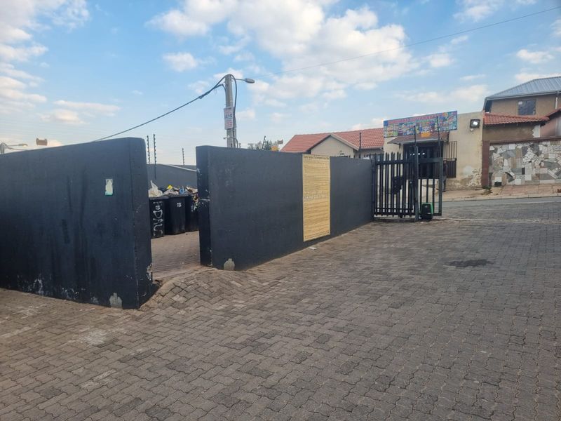 Street view of the property entrance featuring a paved driveway, perimeter wall with security gate, and electric fencing.