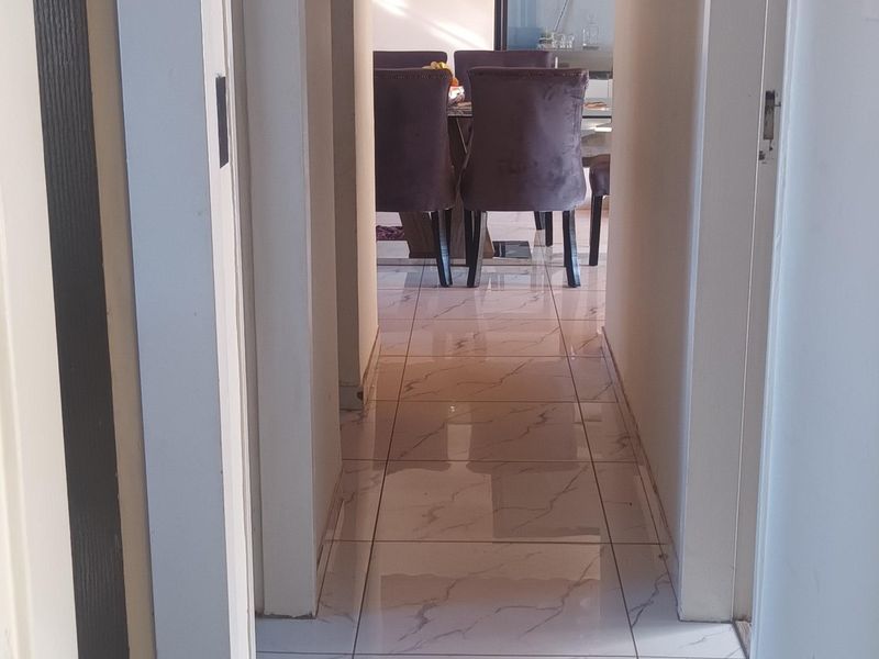 A bright hallway featuring modern marble-look floor tiles and a warm timber-paneled ceiling, leading into the main living area.