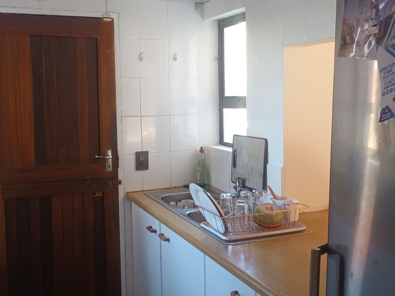 A functional kitchen area featuring a stainless steel sink, tiled splashback, and built-in cabinetry with a wooden door leading to the exterior.