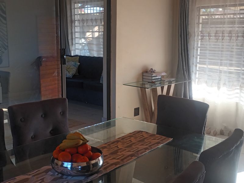 A dining area featuring tiled flooring and a sliding glass door leading to an adjacent living space with security bars on the windows.