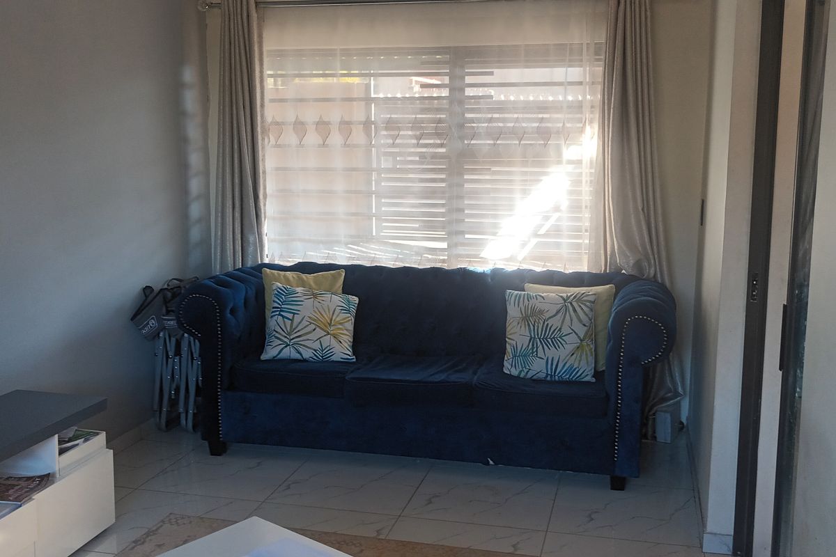 A comfortable living room featuring tiled flooring and large windows with venetian blinds and curtains, providing natural light to the space.
