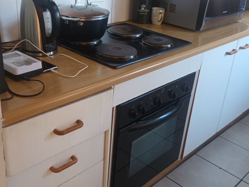 A functional kitchen featuring a built-in oven, electric hob, laminate countertops, and tiled flooring with white cabinetry.