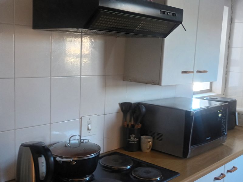 A functional kitchen featuring built-in cabinetry, a tiled backsplash, laminate countertops, and a fitted extractor fan above the electric hob.