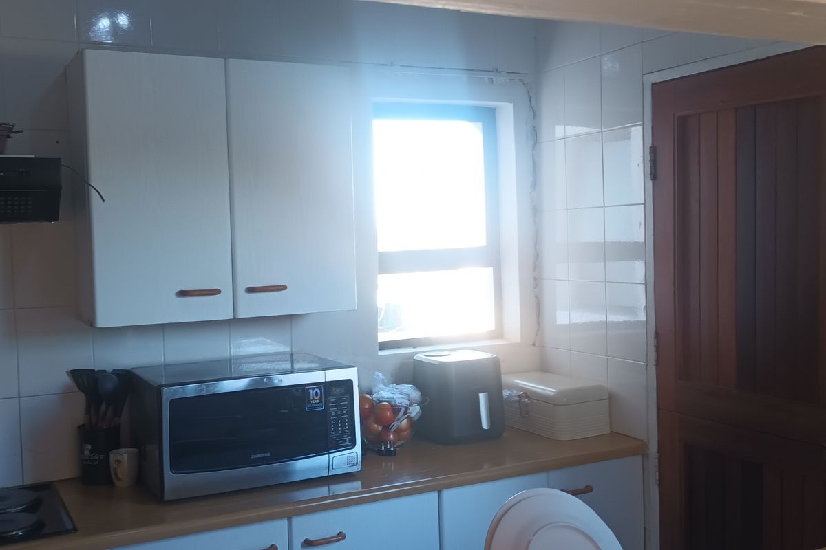 A functional kitchen area featuring white cabinetry, tiled splashbacks, a built-in hob with extractor fan, and a solid timber door.