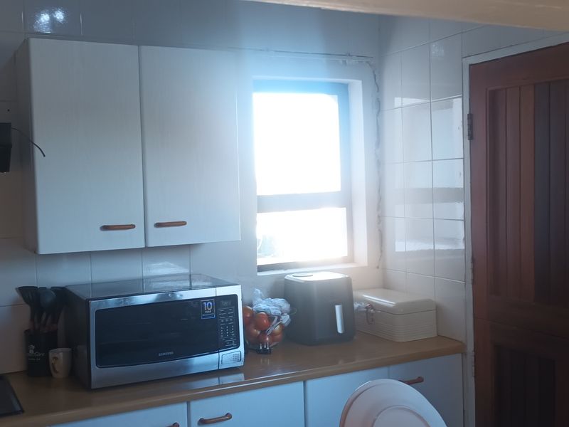A functional kitchen area featuring white cabinetry, tiled splashbacks, a built-in hob with extractor fan, and a solid timber door.