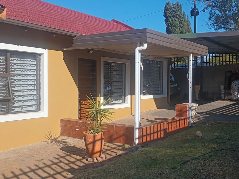 Rear view of the house featuring a tiled patio area, covered carport, and security bars on the windows.