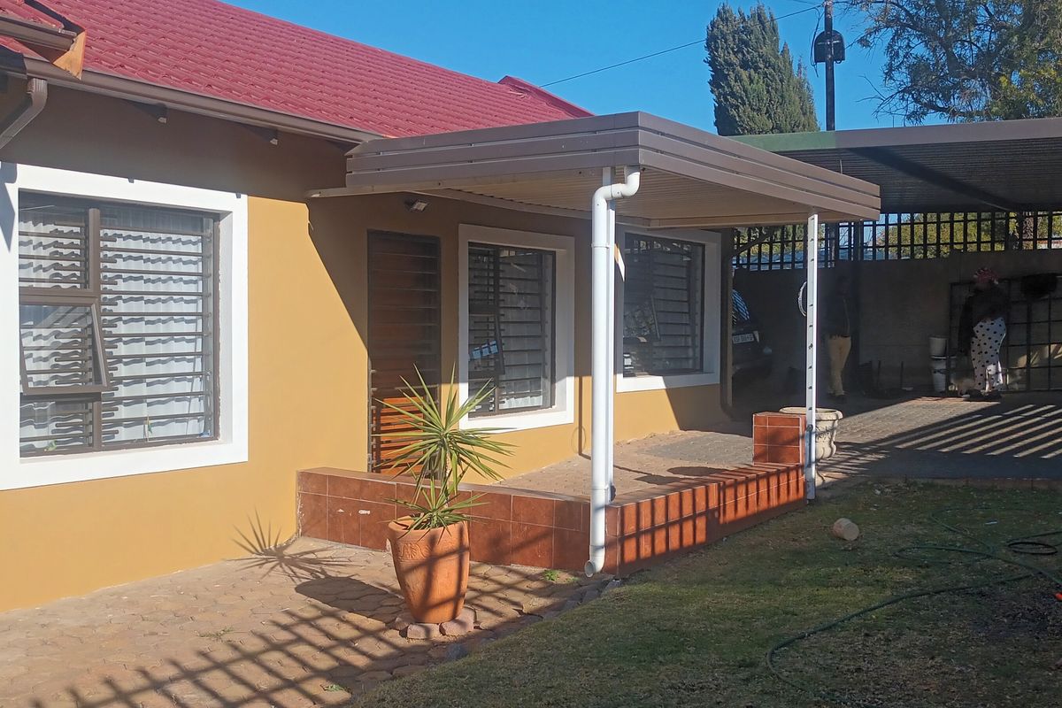 Rear view of the house featuring a tiled patio area, covered carport, and security bars on the windows.