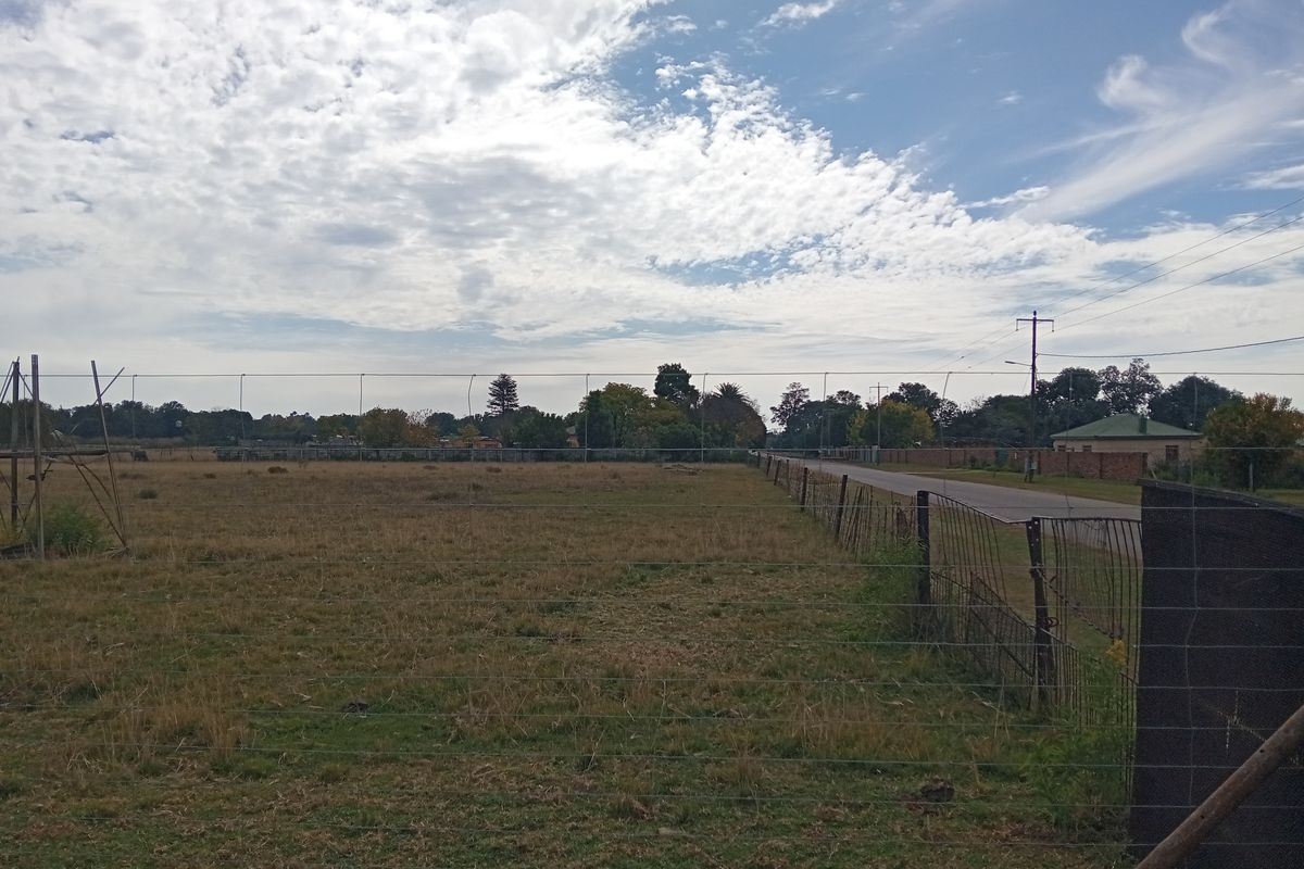 A wide-angle view of an open farm pasture bordered by wire fencing and adjacent to a rural road.