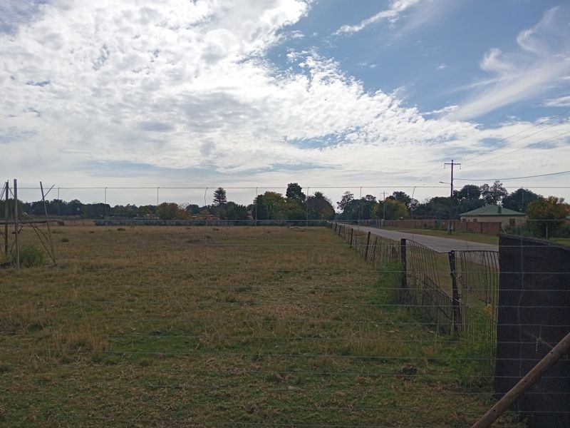 A wide-angle view of an open farm pasture bordered by wire fencing and adjacent to a rural road.