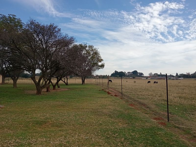 A view of the farm property featuring open grassland, mature trees, and perimeter wire fencing.