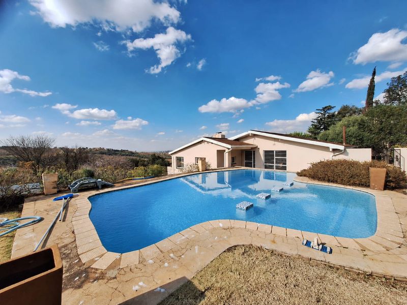 A rear exterior view featuring a swimming pool with built-in steps, set against a paved deck and a residential building structure.