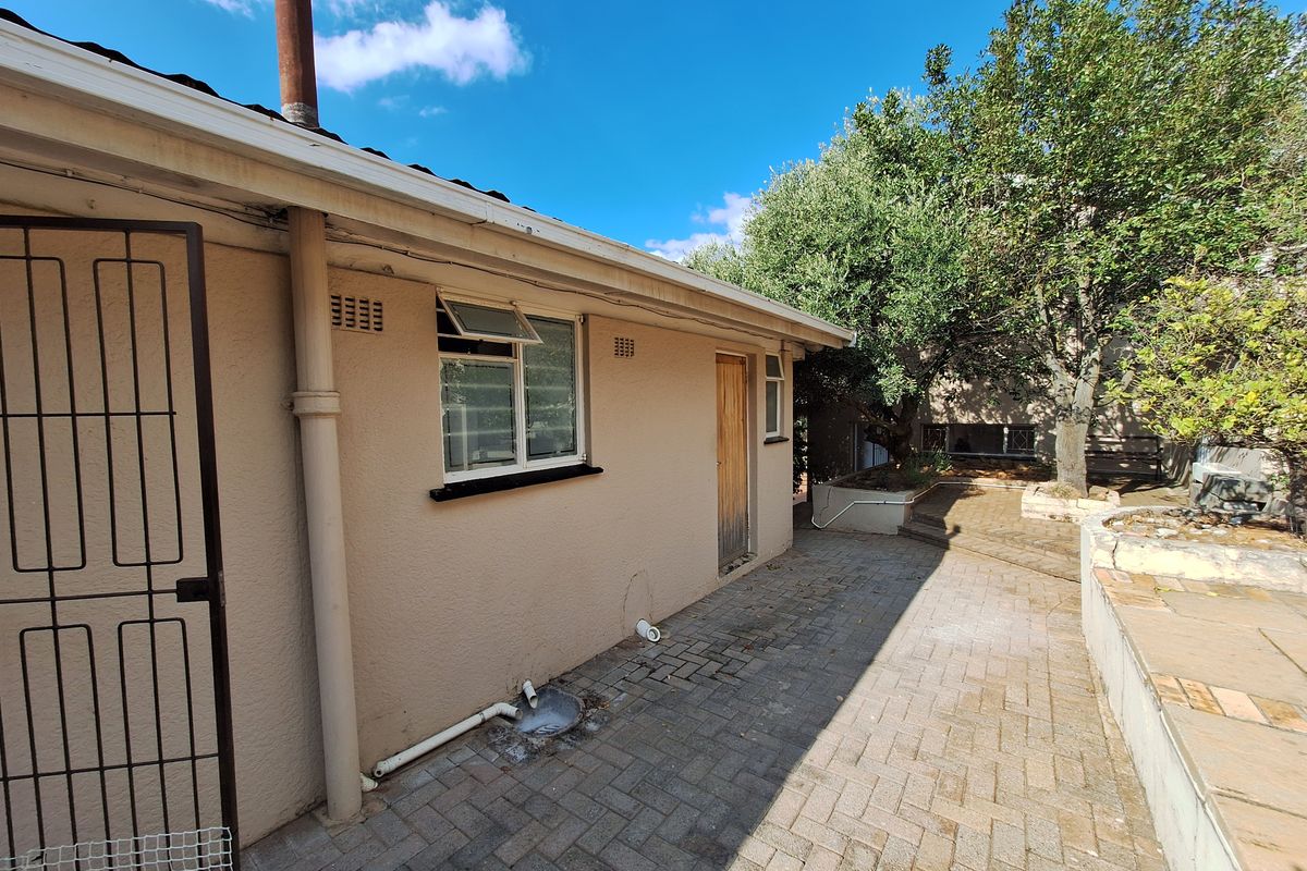 Rear exterior view of the property featuring a paved patio area, security gate, and established garden surroundings.