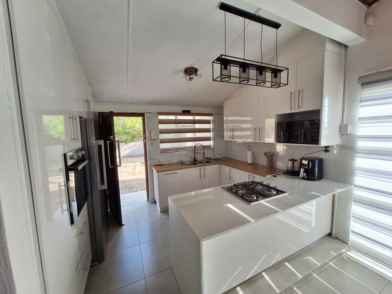 Modern kitchen featuring high-gloss cabinetry, stone countertops, integrated gas hob, built-in oven, and microwave, with direct access to the outdoor area.