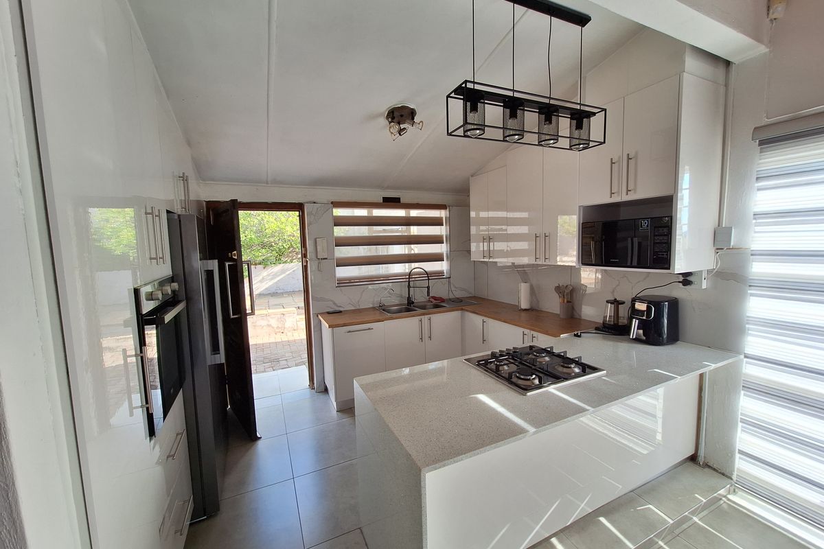 Modern kitchen featuring high-gloss cabinetry, stone countertops, integrated gas hob, built-in oven, and microwave, with direct access to the outdoor area.
