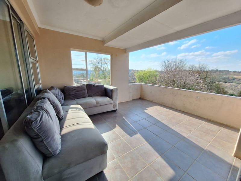 A covered balcony featuring tiled flooring and a concrete balustrade, offering an open-air space with views of the surrounding landscape.