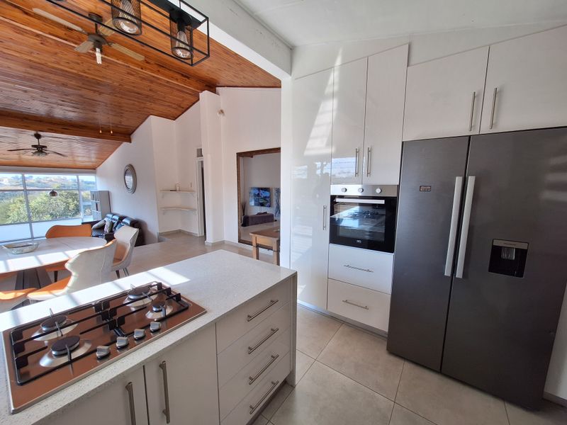 Modern open-plan kitchen featuring high-gloss cabinetry, stone countertops, and a gas cooktop, seamlessly flowing into a spacious living area with vaulted timber ceilings.