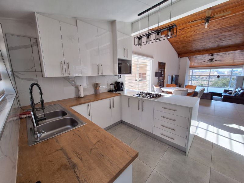 Modern open-plan kitchen featuring high-gloss cabinetry, wood and stone countertops, and a gas hob, flowing into a spacious living area with timber ceilings.