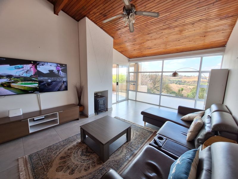 Spacious living room featuring a vaulted timber ceiling, cast iron fireplace, and expansive floor-to-ceiling windows offering scenic views and access to the patio.