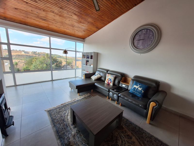 Spacious living room featuring a vaulted timber ceiling, large windows with scenic views, tiled flooring, and a built-in fireplace.