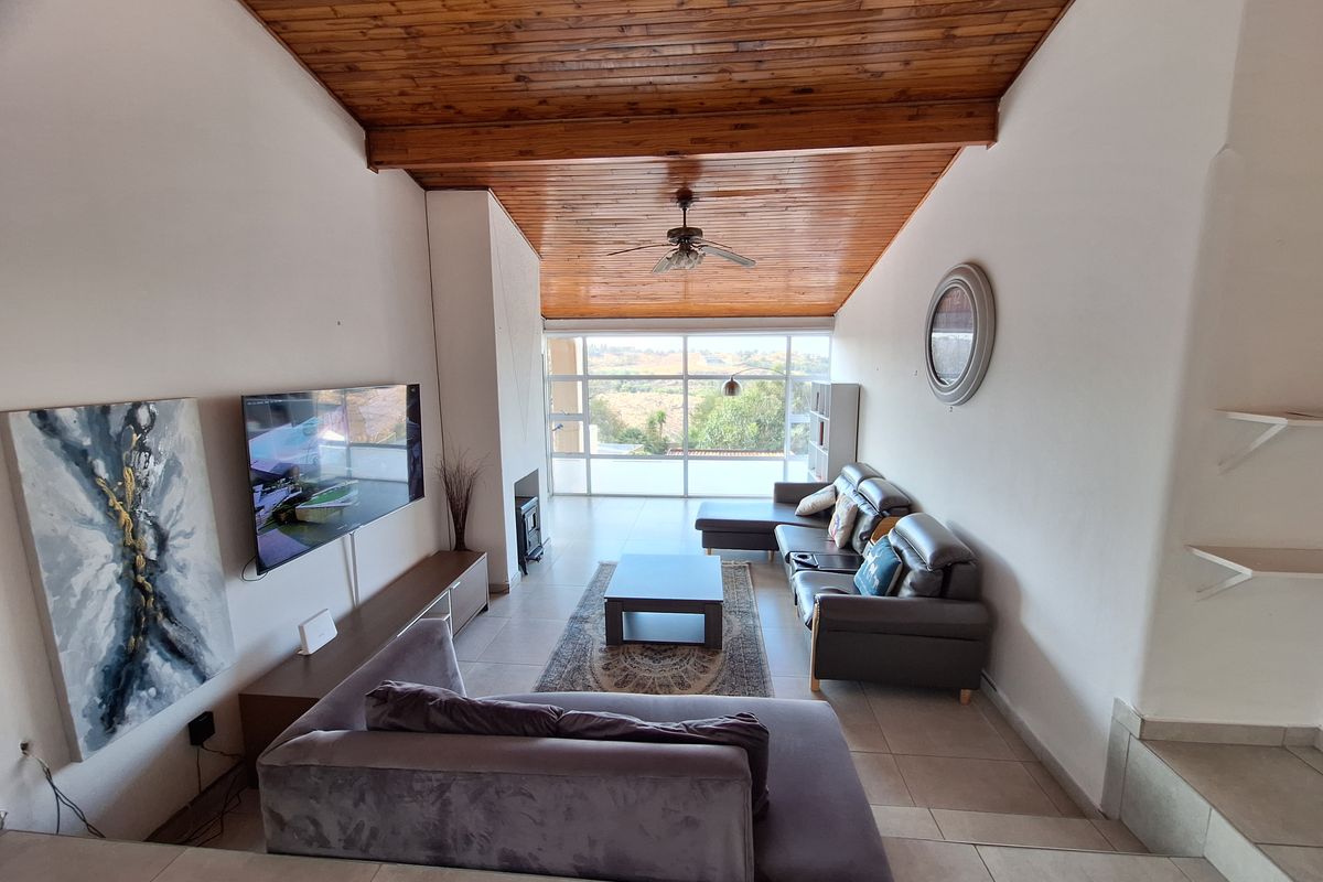 Spacious living room featuring a vaulted timber-clad ceiling, tiled floors, and a large window wall offering natural light and scenic views.