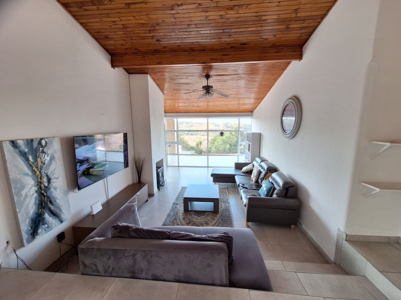 Spacious living room featuring a vaulted timber-clad ceiling, tiled floors, and a large window wall offering natural light and scenic views.