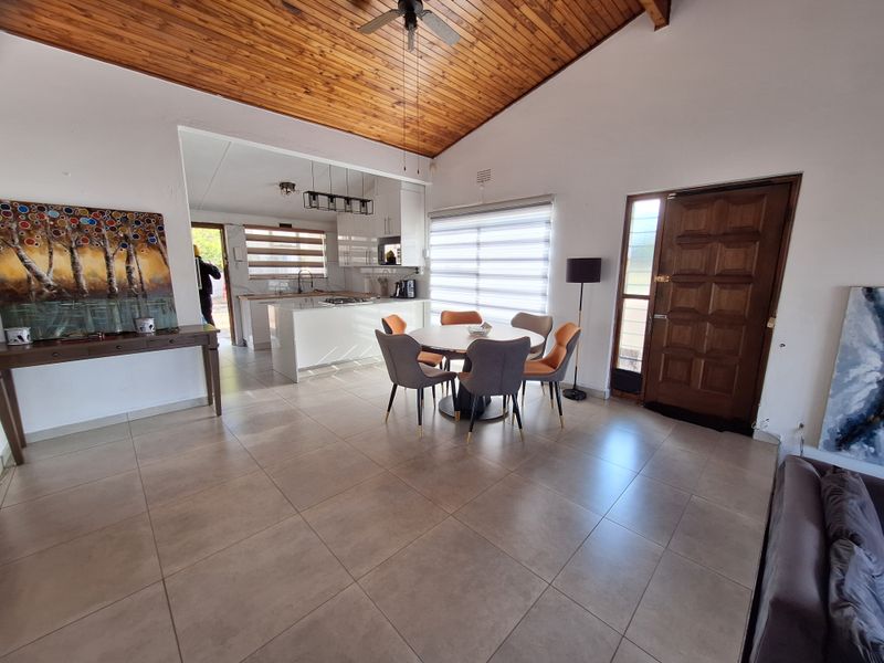 Spacious open-plan living and dining area featuring a high timber vaulted ceiling, tiled flooring, and a modern kitchen with a central island.