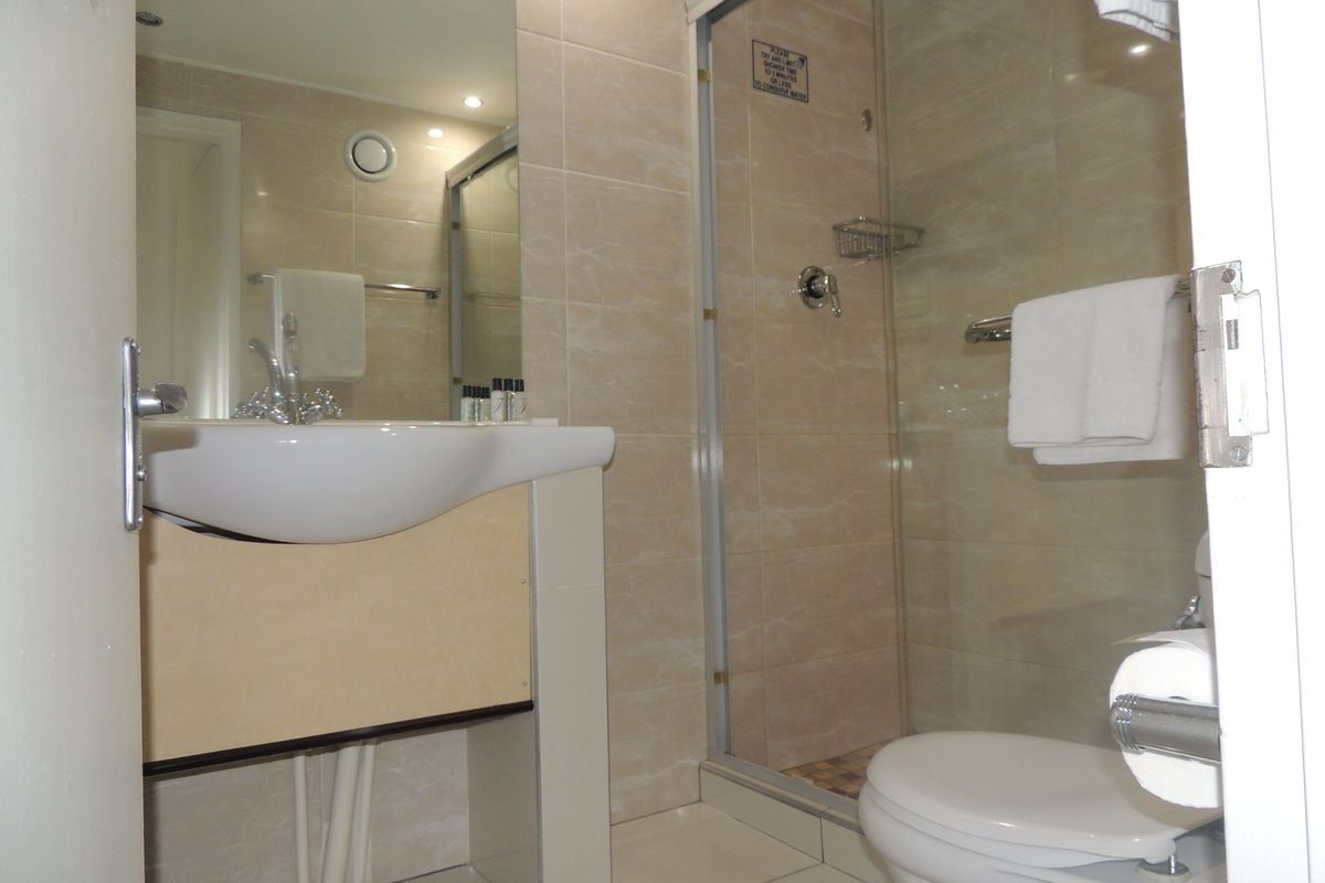 A functional bathroom featuring a glass-enclosed shower, wall-mounted basin, and neutral tiled finishes throughout.
