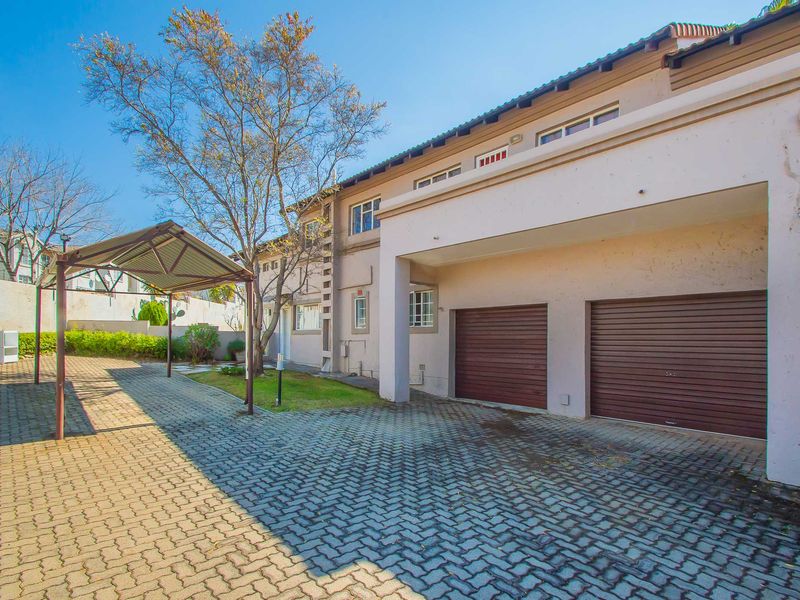 Front exterior view of the apartment featuring a paved driveway, double garage, and an additional carport structure.