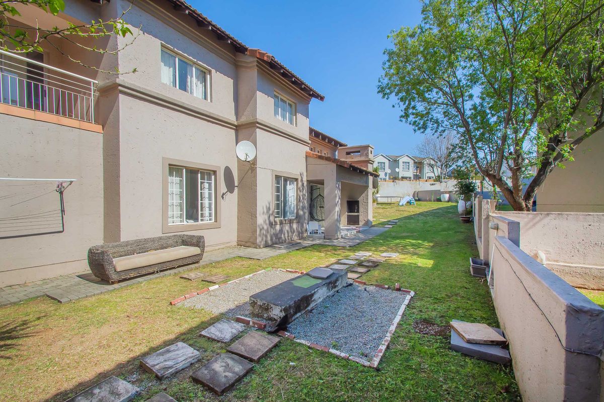Rear exterior view of the apartment featuring a private garden, paved patio area, and a built-in braai facility.