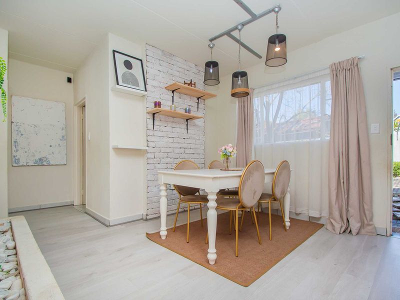 A bright dining area featuring an exposed brick accent wall, modern pendant lighting, and light-toned laminate flooring with direct access to the exterior.