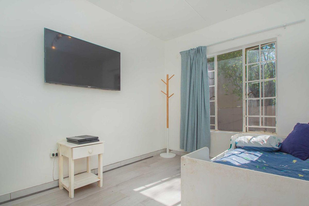 A bedroom featuring light-toned laminate flooring, white walls, and a grid-style window allowing natural light into the space.