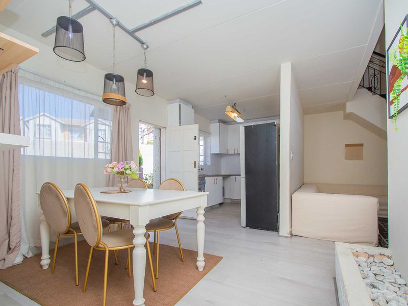 Open plan living and dining area featuring laminate flooring, a compact kitchen with built-in cabinetry, and an internal staircase.