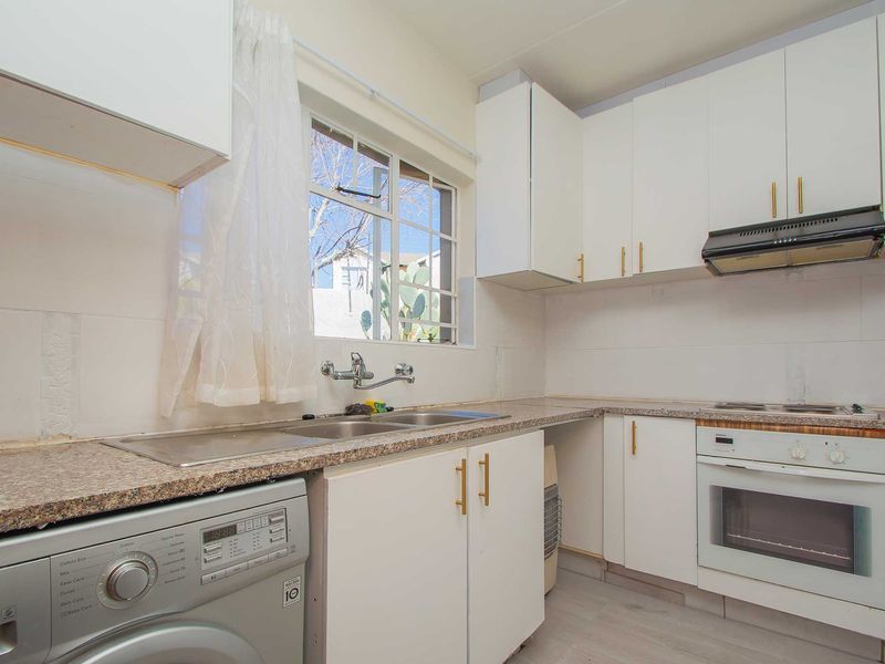 Functional kitchen featuring white cabinetry, laminate countertops, built-in oven, hob, extractor fan, and a double bowl sink with a window view.